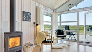 A cozy room with a wood-burning stove, a dining area with chairs and a table, and large windows offering a view of the outdoors. - "Chrisse" - 550m from the sea by Interhome (Rømø)