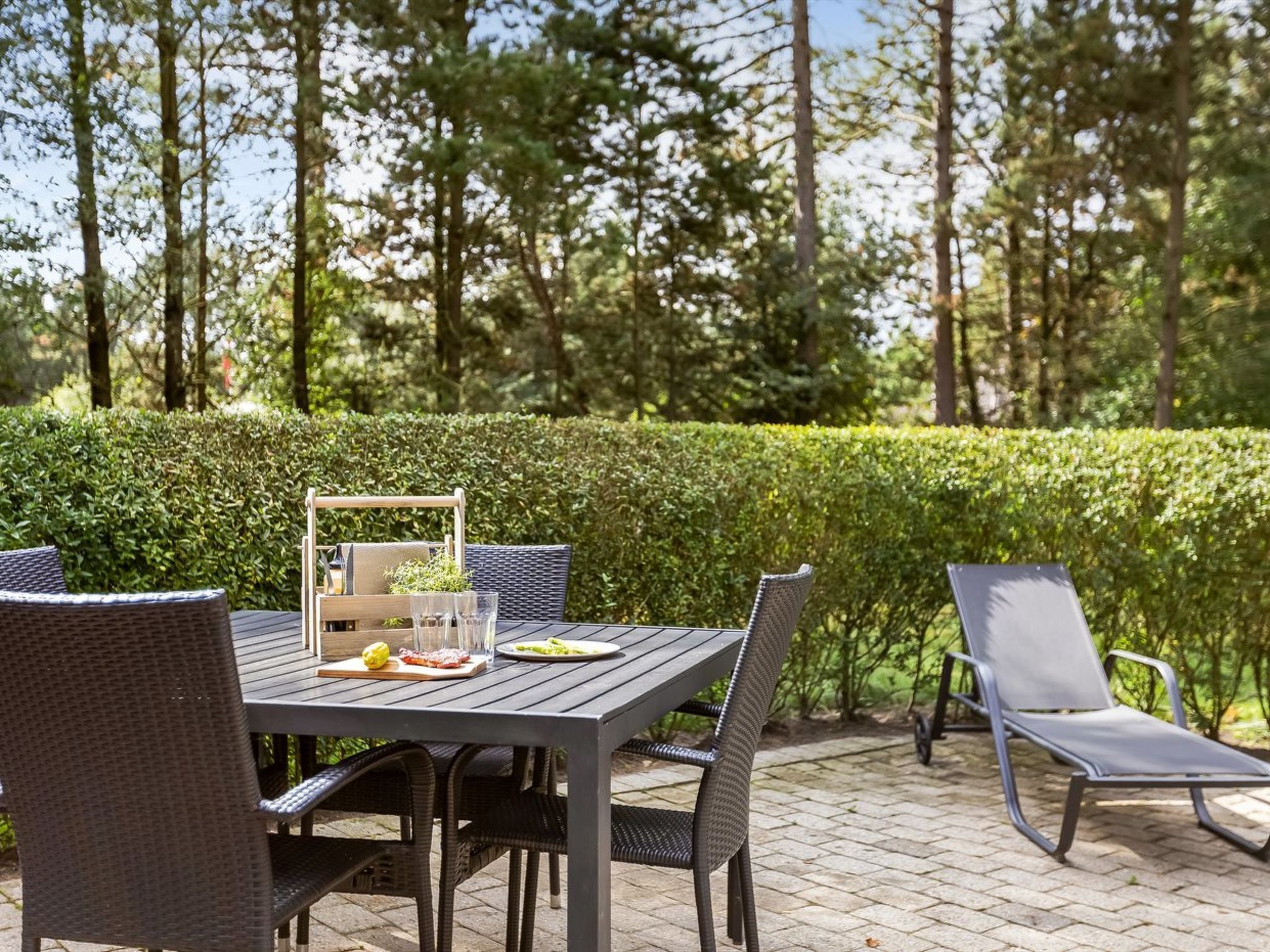 An outdoor patio with a table set for two, surrounded by wicker chairs.