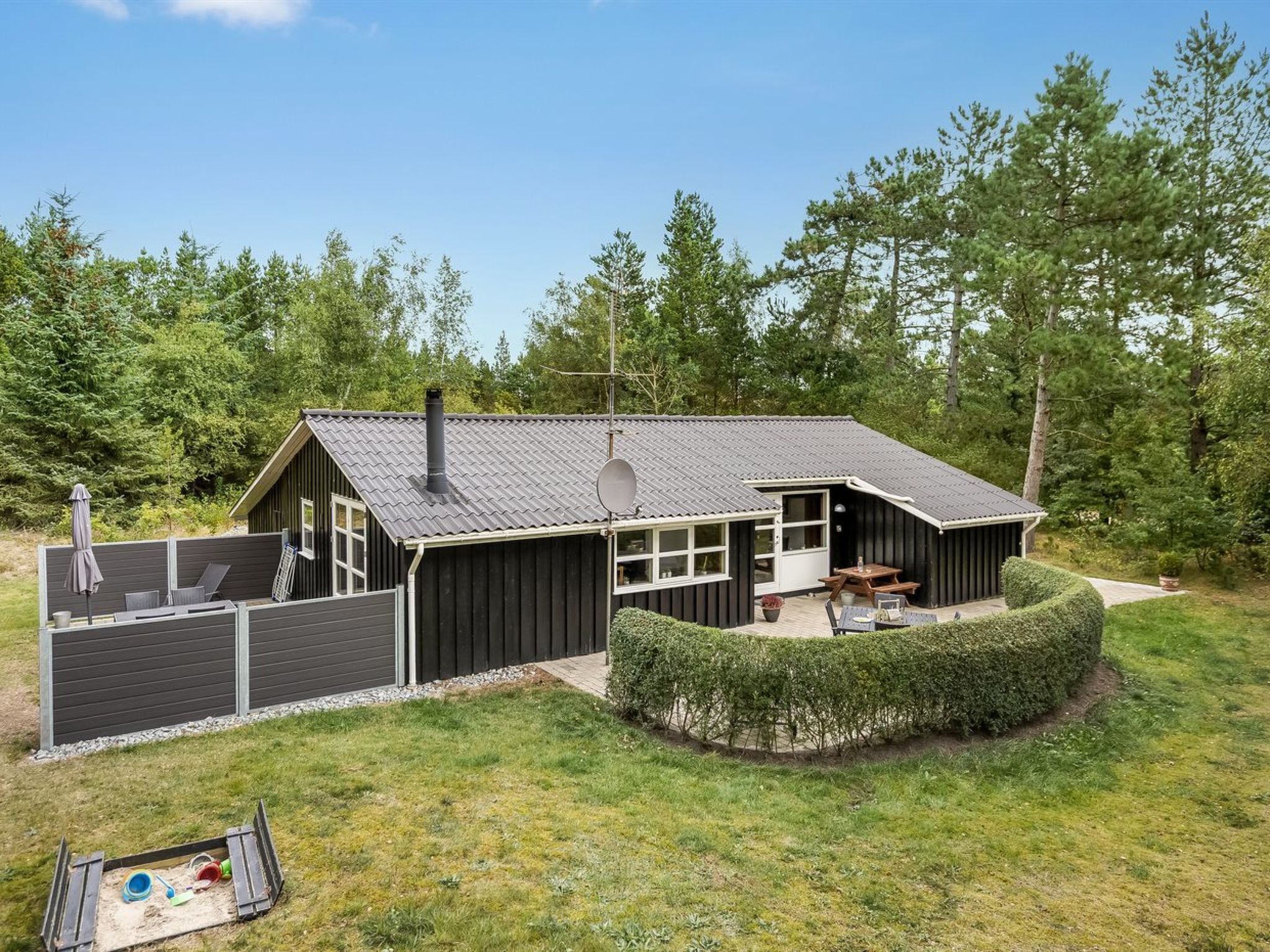 A cabin with a large deck, a covered patio, and a fenced play area.