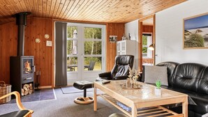 Un salon chaleureux avec une cheminée, des meubles en cuir et une vue sur l’extérieur grâce à une porte vitrée.