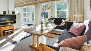 Un salon moderne avec un plafond en bois, de grandes fenêtres, un canapé, une table basse et un téléviseur.