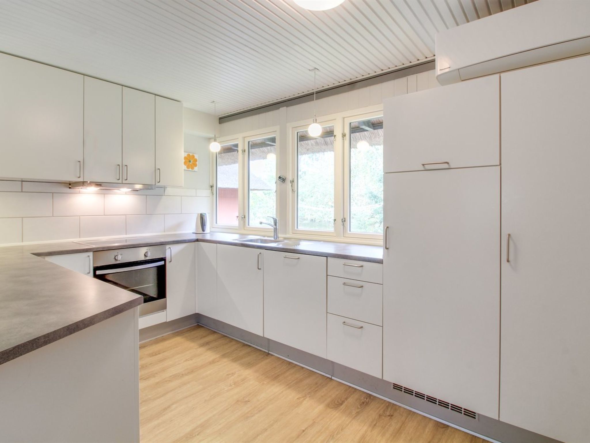 Eine moderne Küche mit weißen Schränken, einer Holz Arbeitsplatte, einem eingebauten Ofen und einem Fenster mit Blick auf Grünflächen.