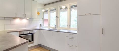 A modern kitchen with white cabinets, a wooden countertop, a built-in oven, and a window with a view of greenery.