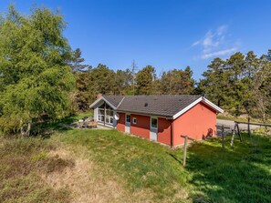 Et lille rødt hus med skrå tag, veranda og parabol.