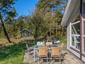 Eine Terrasse mit Tisch, Stühlen, einem Grill und einem Haus im Hintergrund.