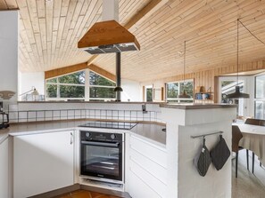Una cocina moderna con horno empotrado, techo de madera y ventanas amplias.
