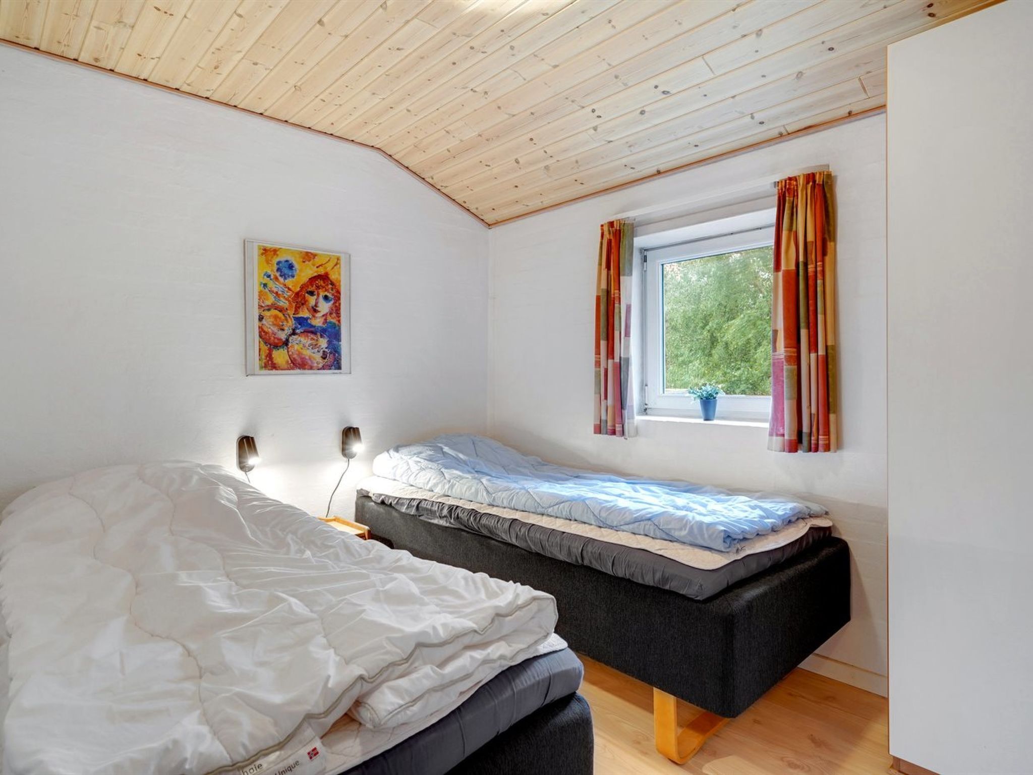 Une chambre avec deux lits, une fenêtre avec des rideaux, un tableau au mur et une lampe de chevet.