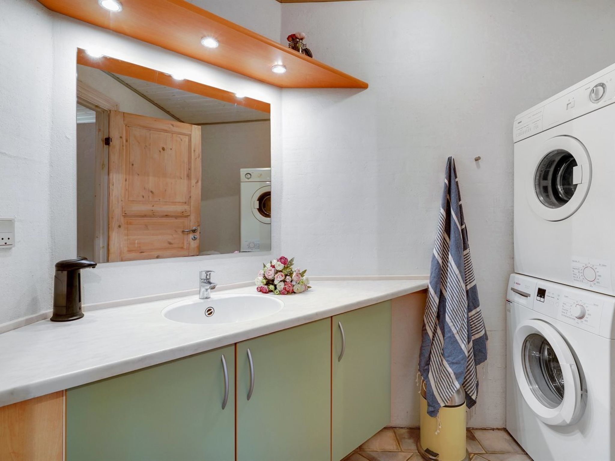 A modern bathroom with a sink, mirror, wooden cabinets, a washing machine, and a towel rack.