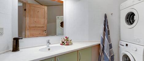 A modern bathroom with a sink, mirror, wooden cabinets, a washing machine, and a towel rack.