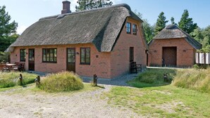 Et traditionelt stråtækt hus med murstensfacade, et mindre tilbygget rum og en grusvej, der fører til indgangen.