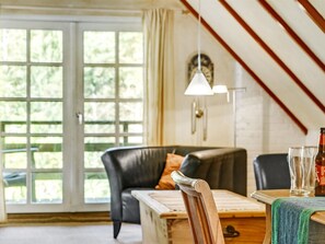 Ein gemütliches Wohnzimmer mit einem Holztisch, einer schwarzen Ledersofa und einem Fenster mit Blick auf Grünflächen.