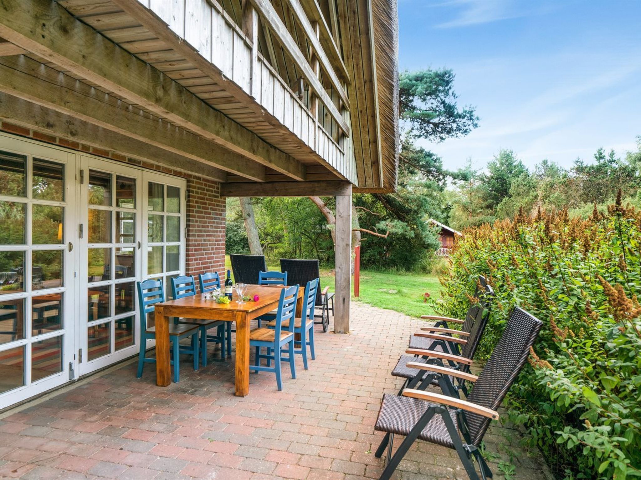 Eine Terrasse im Freien mit einem Holztisch und Stühlen, einem überdachten Sitzbereich und einem Boden aus Ziegelsteinen.