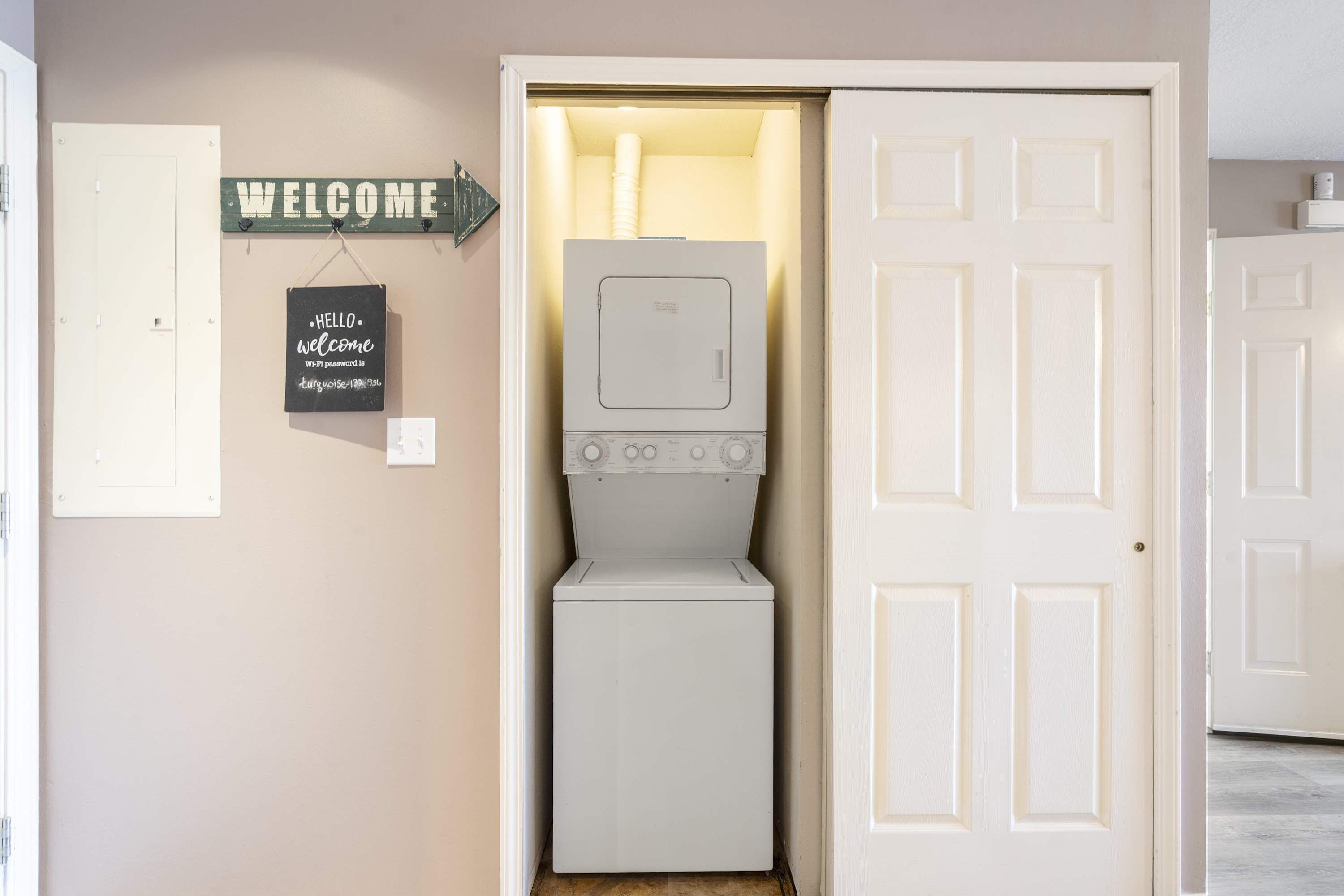A laundry room with a washing machine and dryer, a welcome sign, and a door to another room.
