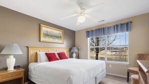 Una camera da letto con un letto grande, un ventilatore a soffitto, una finestra con vista e un comodino con una lampada.