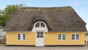 Ein gelbes Gebäude mit einem Reetdach und einer weißen Tür, beschriftet mit der Nummer 44.