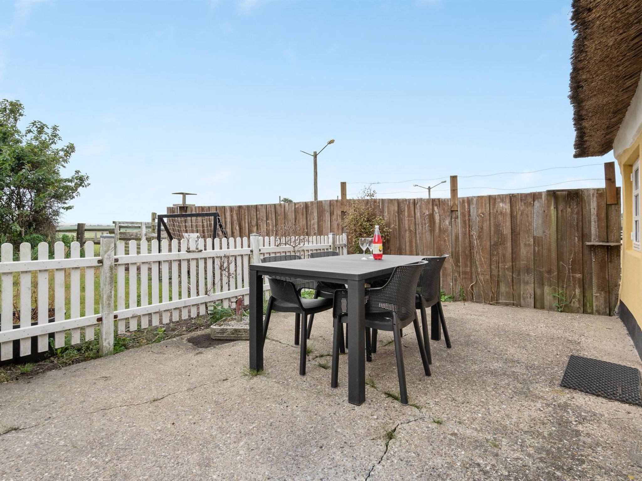 Une terrasse avec une table et des chaises, une bouteille d’eau et un verre.