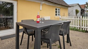 Ein Tisch mit Stühlen und einer Wasserflasche vor einem gelben Gebäude mit einem Strohdach.