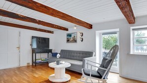 Ein geräumiges Wohnzimmer mit grauem Sofa, einem weißen Schaukelstuhl, einem runden Couchtisch und einem Flachbildfernseher.