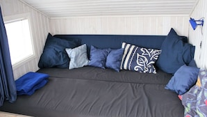 Un sofá acogedor de color oscuro con varios cojines en una habitación con paredes de paneles blancos y un ventanal.