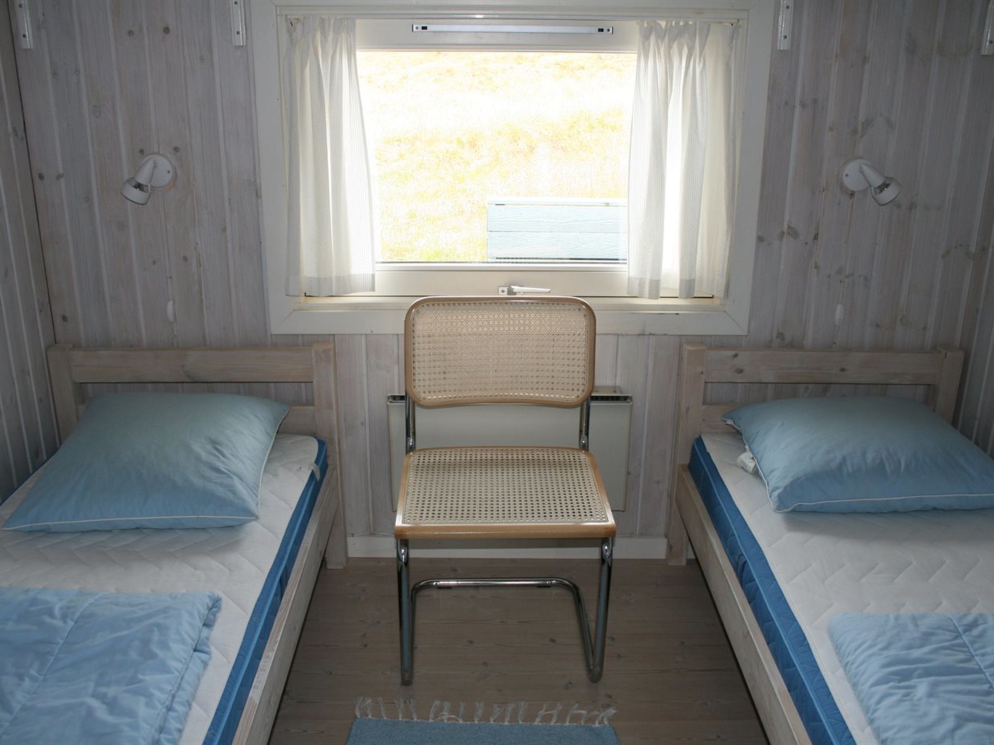 A room with two single beds, a central chair, and a window with curtains.