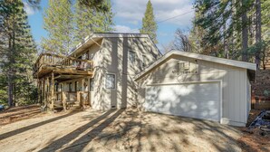 A two-story house with a deck, garage, and a forested backdrop. - Deck & Gas Grill: Secluded Arnold Cabin Rental! (Arnold)