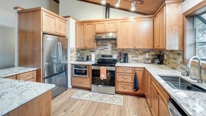 A modern kitchen with wooden cabinets, stainless steel appliances, and a large window. - Deck & Gas Grill: Secluded Arnold Cabin Rental! (Arnold)