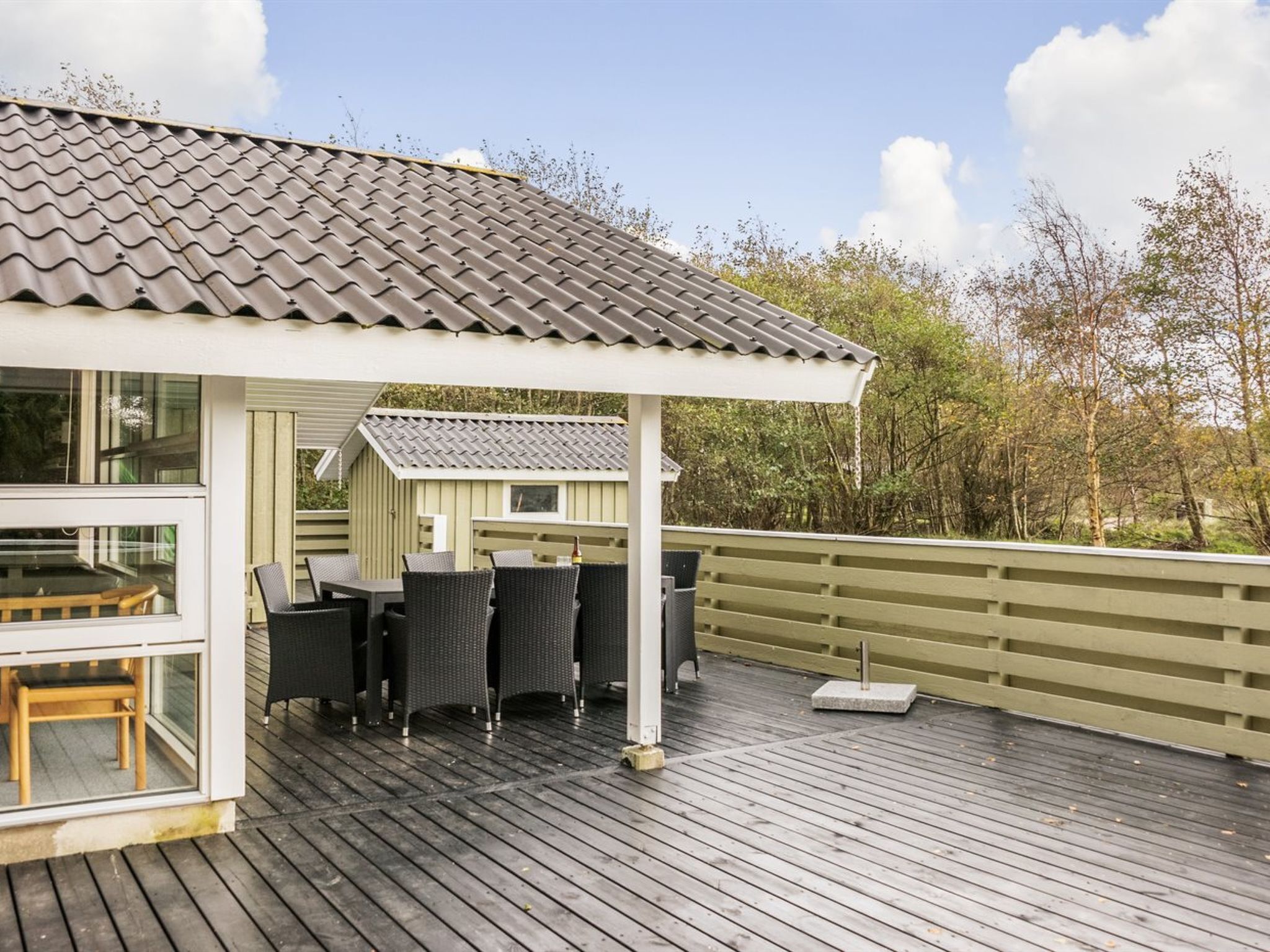 A wooden deck with outdoor furniture, a pergola, and a view of trees.