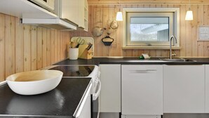 A modern kitchen with wooden paneling, a black countertop, a white bowl, a knife block, and a window with a view. - "Nanne" - 1km from the sea by Interhome (Fanø)