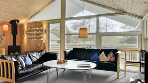 A cozy living room with a fireplace, a sofa, a coffee table, and large windows offering a view of the outdoors. - "Nanne" - 1km from the sea by Interhome (Fanø)