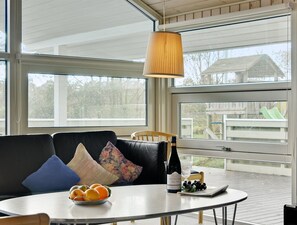 Un salon moderne avec un canapé en cuir noir, une table ronde sur laquelle se trouve une bouteille de vin, un saladier rempli de fruits et une suspension décorative.