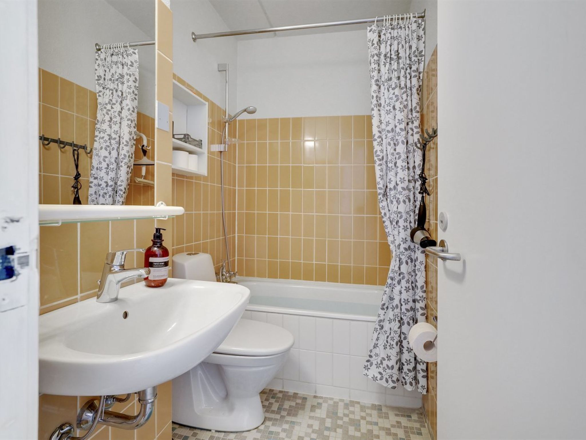 A bathroom with a white sink, toilet, and bathtub. There is a shower curtain with a floral pattern, and a towel rack is visible.