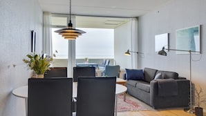 A modern living room with a grey sofa, a dining table with chairs, a large window, and a floor lamp. - "Edelina" - 50m from the sea by Interhome (Fanø)