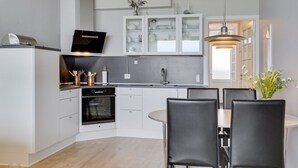 A modern kitchen with white cabinetry, a built-in oven, and a dining area with black chairs. - "Edelina" - 50m from the sea by Interhome (Fanø)