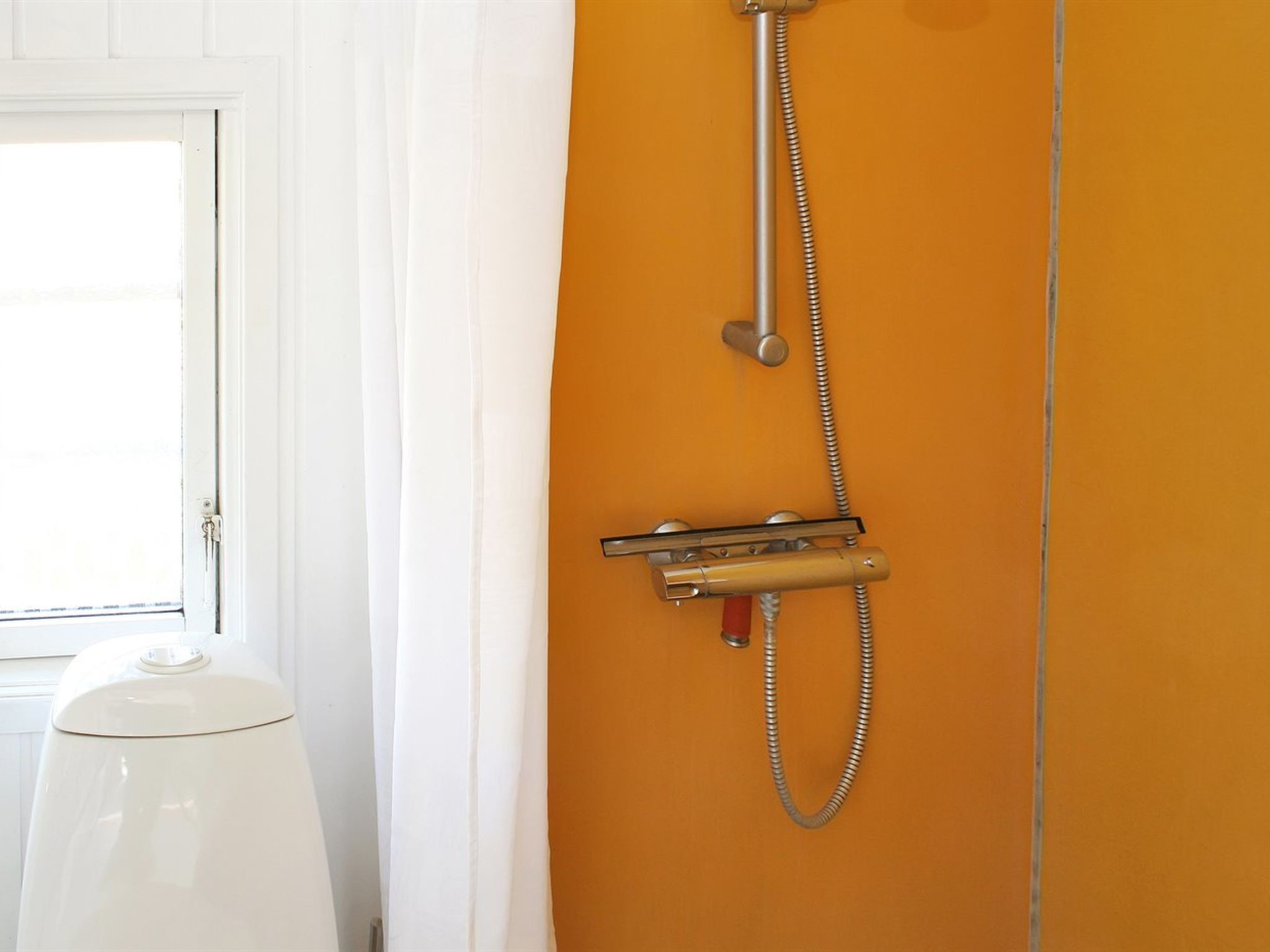 A bathroom with a shower, a toilet, and a window.