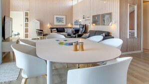 Un salon moderne avec une table ronde blanche, des chaises blanches, un canapé et un téléviseur.
