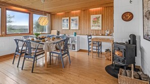 Ein gemütlicher Essbereich mit Holzboden, einem zentralen Tisch und blauen Stühlen. In der Ecke ist ein rustikaler Herd zu sehen.
