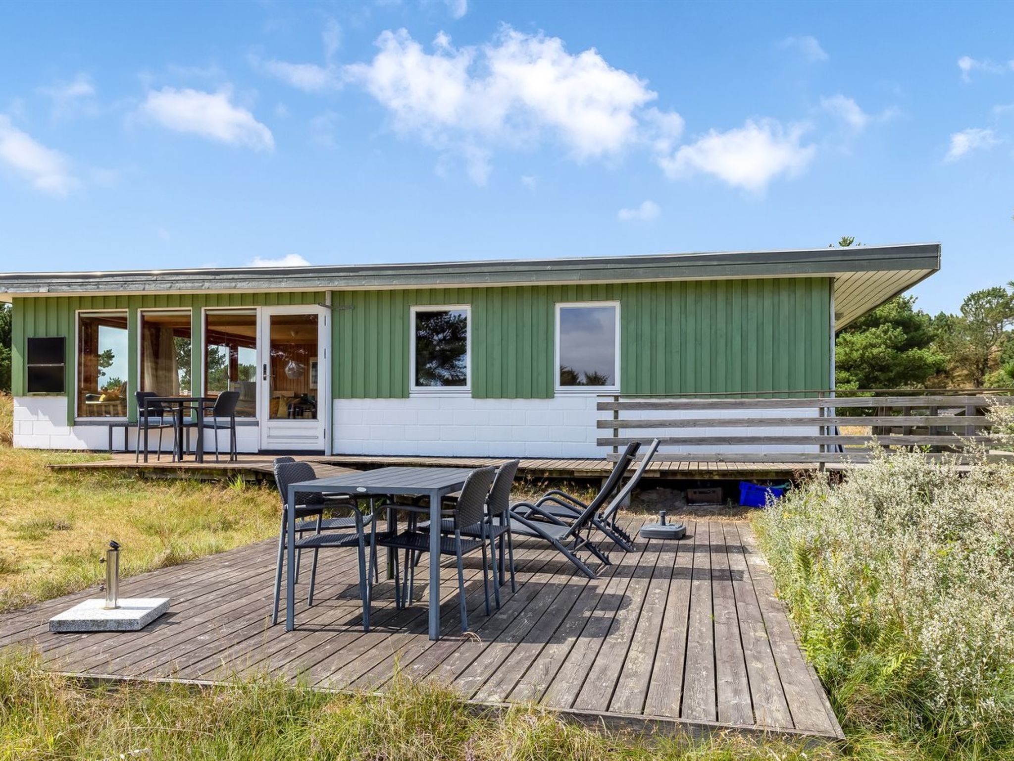 A green mobile home with a deck, outdoor seating, and a small garden area.