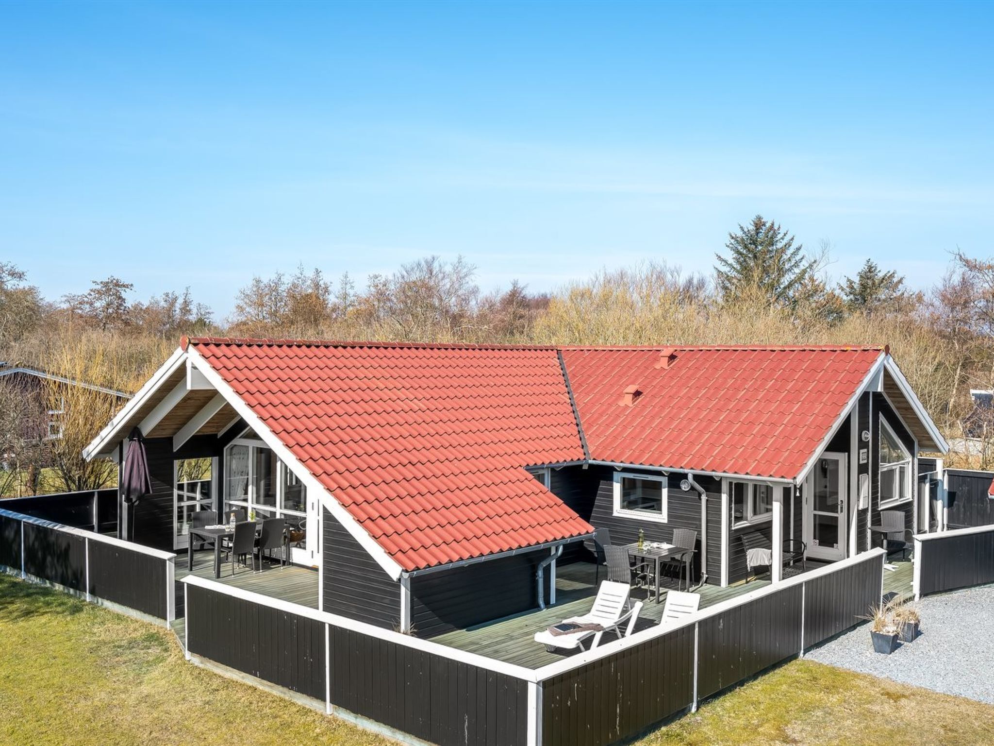 Ett modernt hus med ett rött tak, en täckt uteplats med utemöbler och utsikt över det omgivande landskapet.
