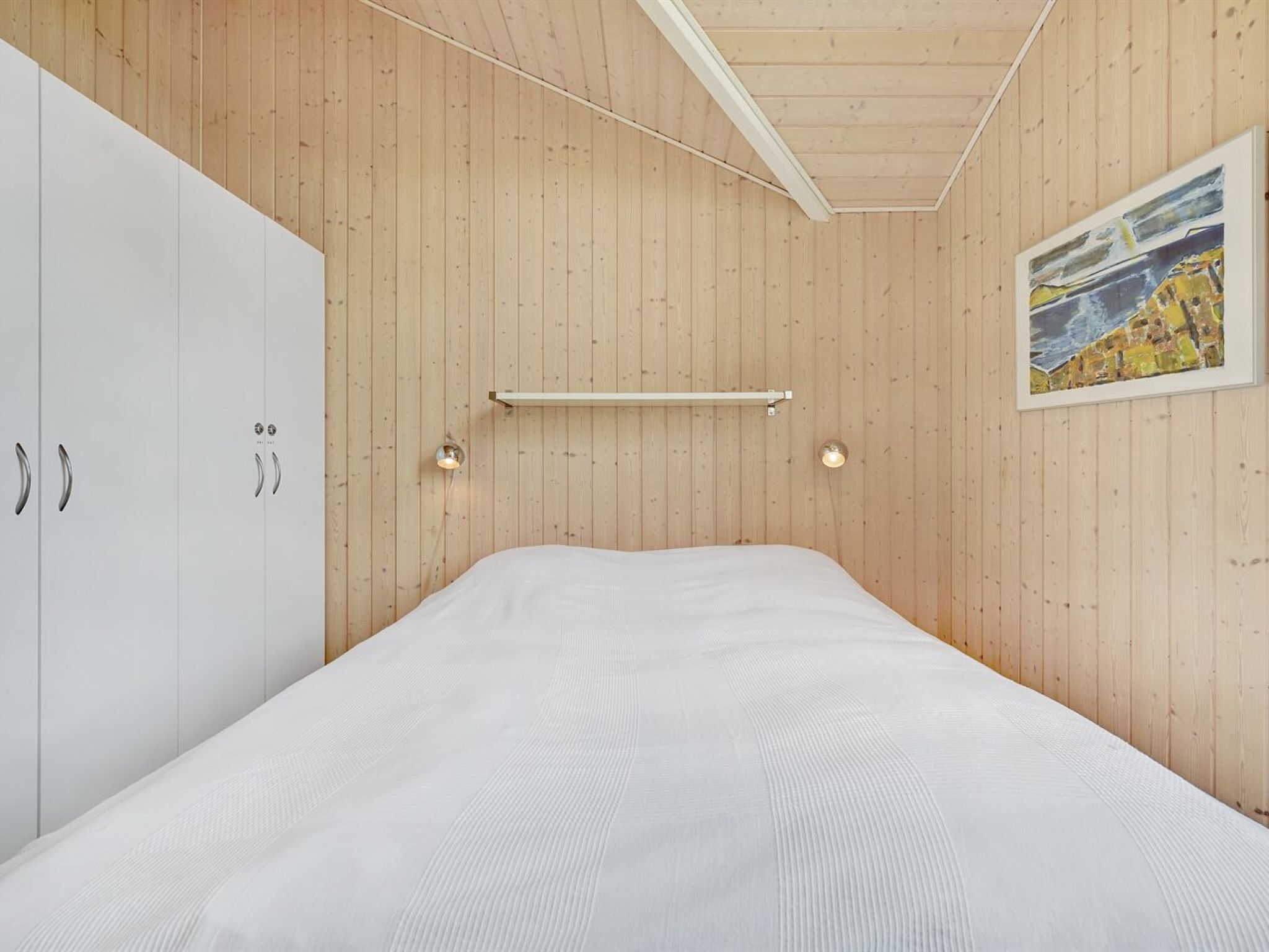 Ein Schlafzimmer mit Holzboden, einem Bett mit weißer Matratze und einem weißen Kleiderschrank.