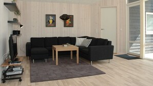 A modern living room with a black sectional sofa, a wooden coffee table, and a grey rug. There are two framed pictures on the wall, a floor lamp, and a TV on a stand. - "Tero" - 450m from the sea by Interhome (Vejers Strand)