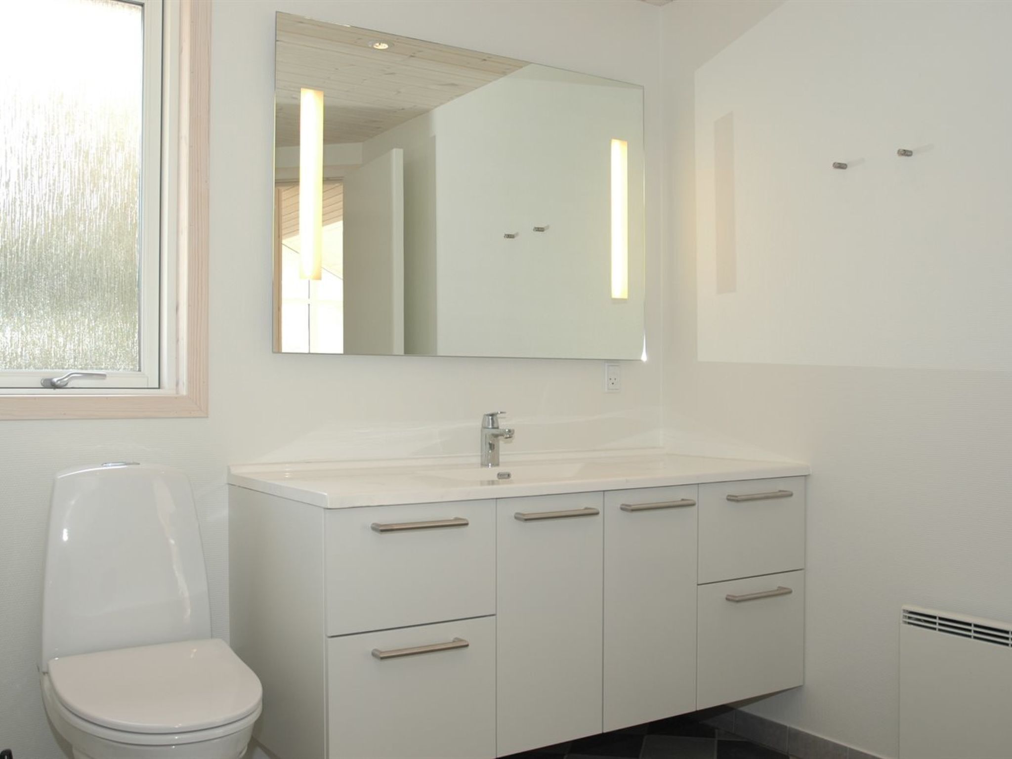 A modern bathroom with a white toilet, a sink with a mirror above it, and a cabinet with drawers.