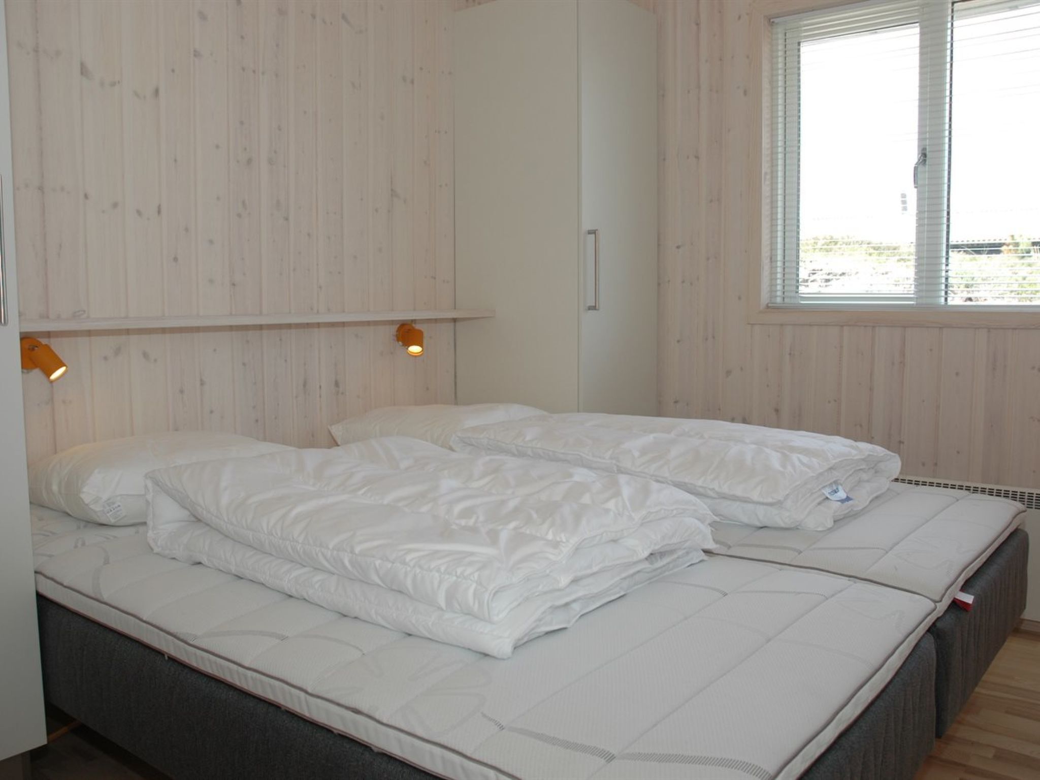 Une chambre avec deux lits, des murs en bois, une fenêtre et un luminaire fixé au mur.