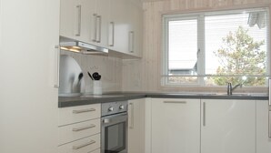 A modern kitchen with white cabinets, stainless steel appliances, and a window with blinds. - "Tero" - 450m from the sea by Interhome (Vejers Strand)