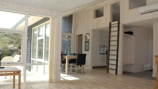 A spacious room with a large sliding glass door leading to an outdoor area, a dining table with chairs, and a kitchen area with a ladder. - "Tero" - 450m from the sea by Interhome (Vejers Strand)