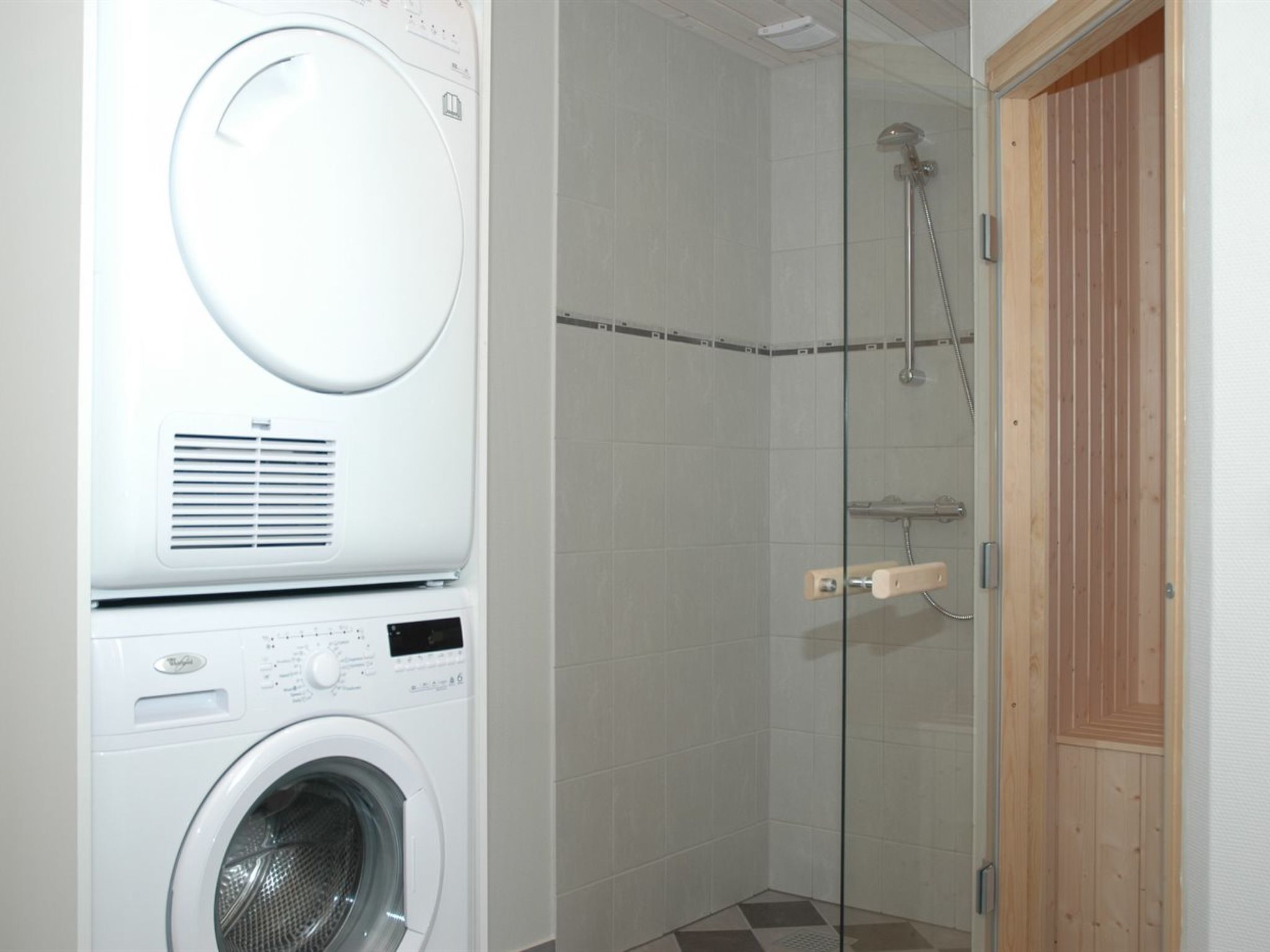 A laundry room with a front-loading washing machine and a glass-enclosed shower area.