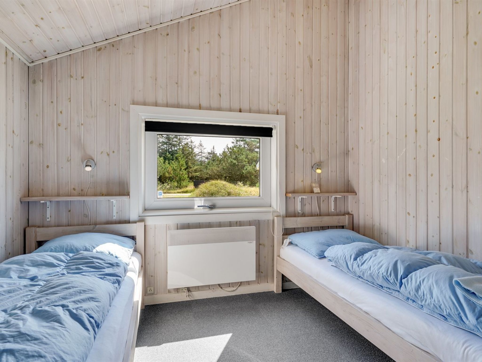 A room with two beds, a TV mounted on the wall, and a window with a view of greenery.