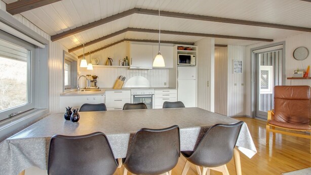 A modern kitchen with white cabinets, a dining table with four chairs, and wooden beams on the ceiling. - "Igilfar" - 700m from the sea by Interhome (Vejers Strand)
