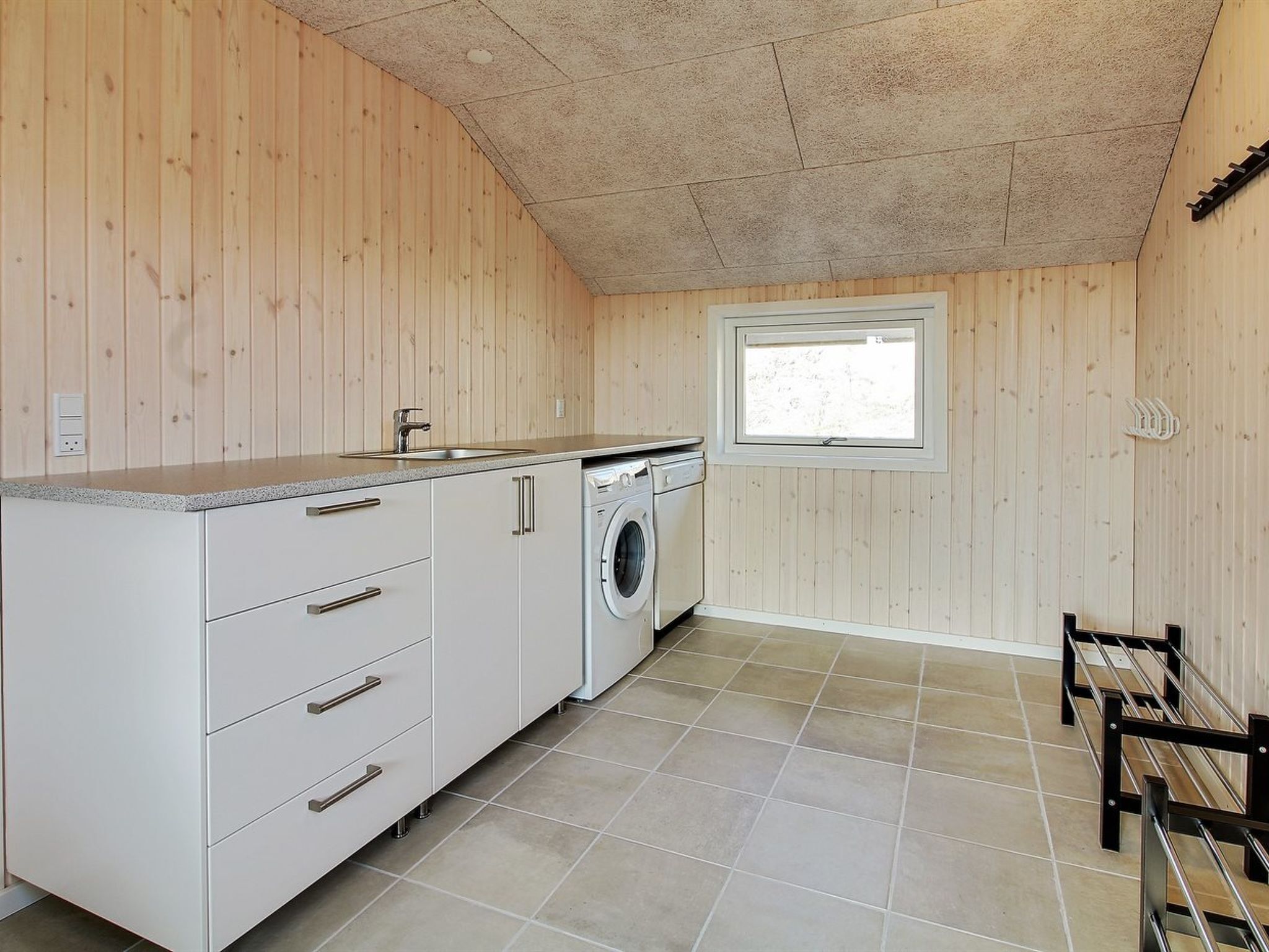 Une cuisine de taille réduite avec des murs en bois, un lave-linge et une fenêtre.