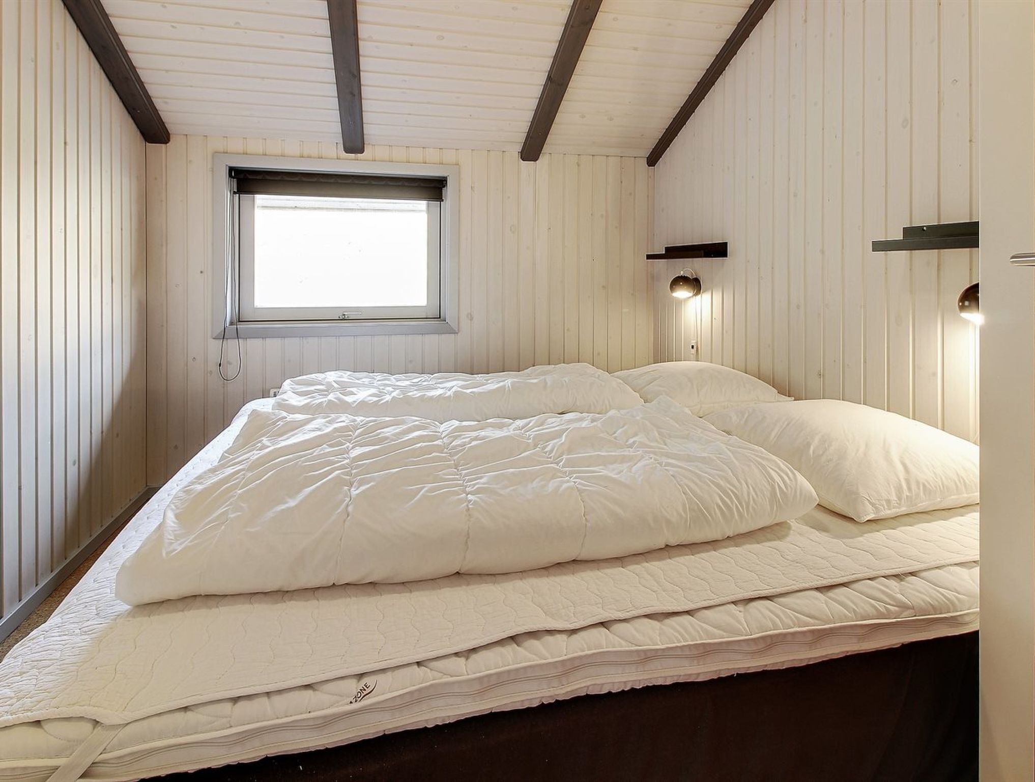 Une chambre avec un grand lit, des murs en bois, une fenêtre et des lampes fixées au mur.