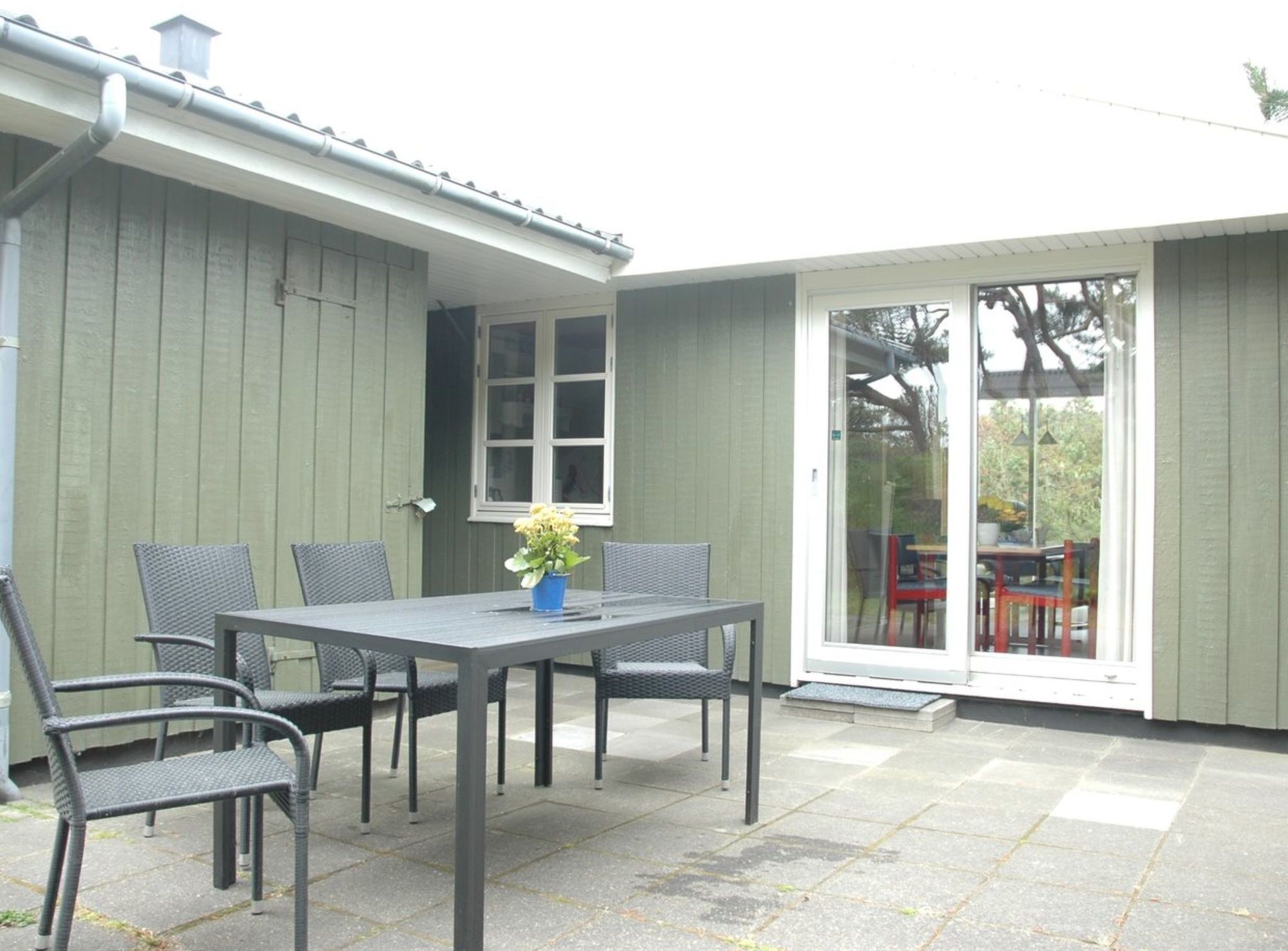 A patio with a table and chairs, a potted plant, and a sliding glass door leading to an outdoor area.